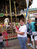 A child holding a stuffed lion in front of a merry-go-round